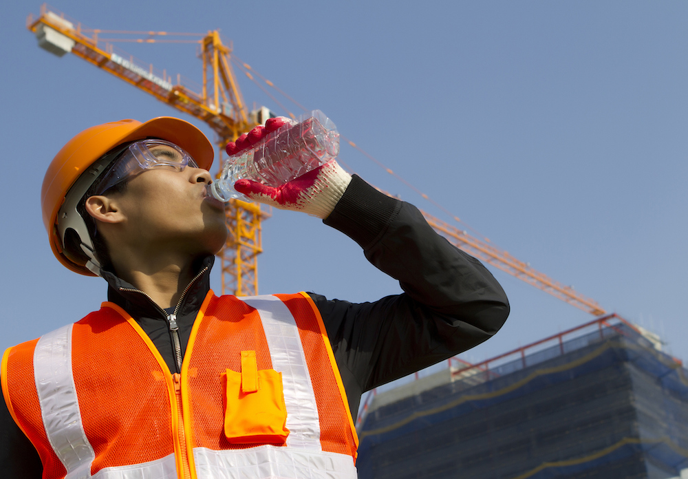 a construction worker takes a break and hydrates on a job site to prevent heat cramps, heat exhaustion, heat stroke, and other heat-related illness